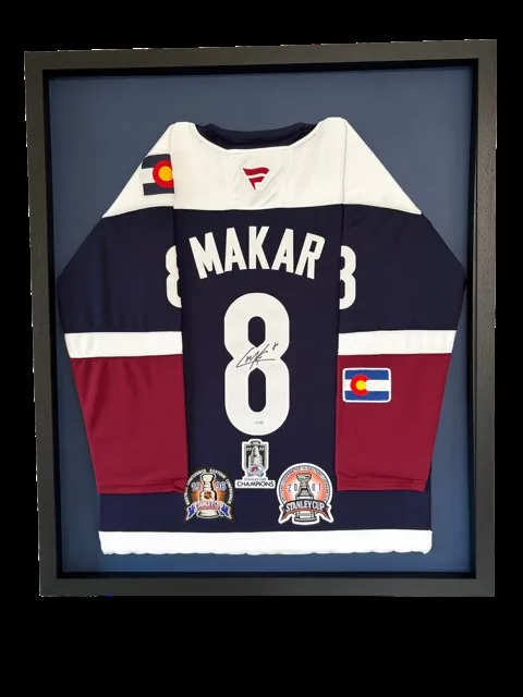 Signed Cale Makar Colorado Avalanche hockey jersey with Stanley Cup patches, framed behind UV glass